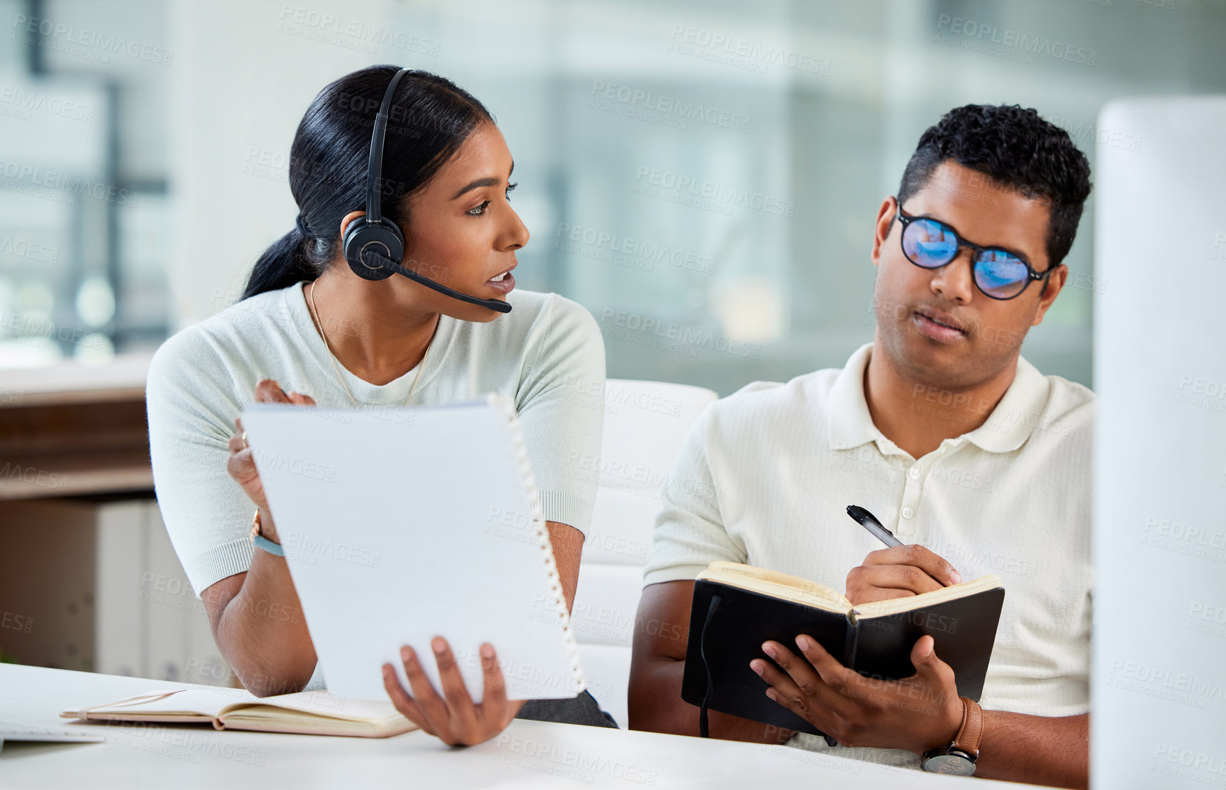 Buy stock photo Shot of an attractive young agent sitting with her trainee in the office and explaining while he writes notes