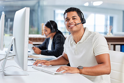 Buy stock photo Shot of two young businesspeople sitting in the office together and wearing headsets while using computers