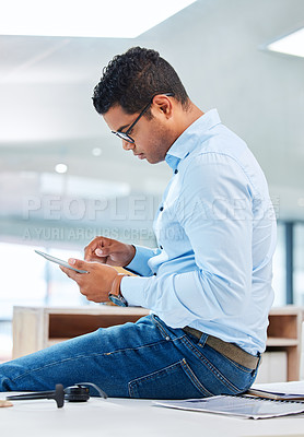 Buy stock photo Shot of a handsome young businessman sitting alone in his office and using a digital tablet