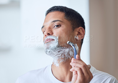 Buy stock photo Shot of a young man shaving his beard in a bathroom at home