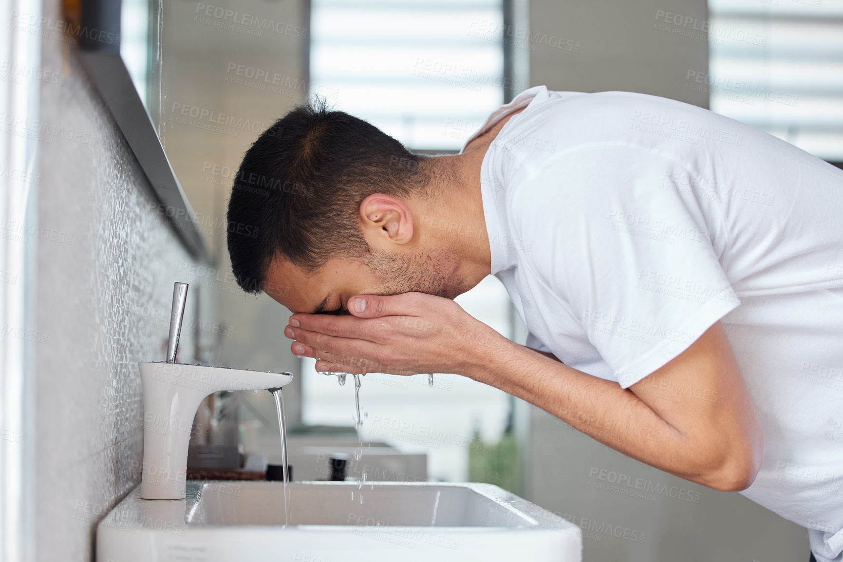 Buy stock photo Shot of a young man washing his face in a bathroom at home