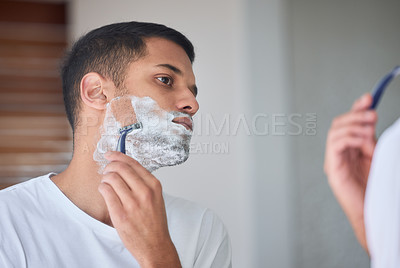 Buy stock photo Shot of a young man shaving his beard in a bathroom at home