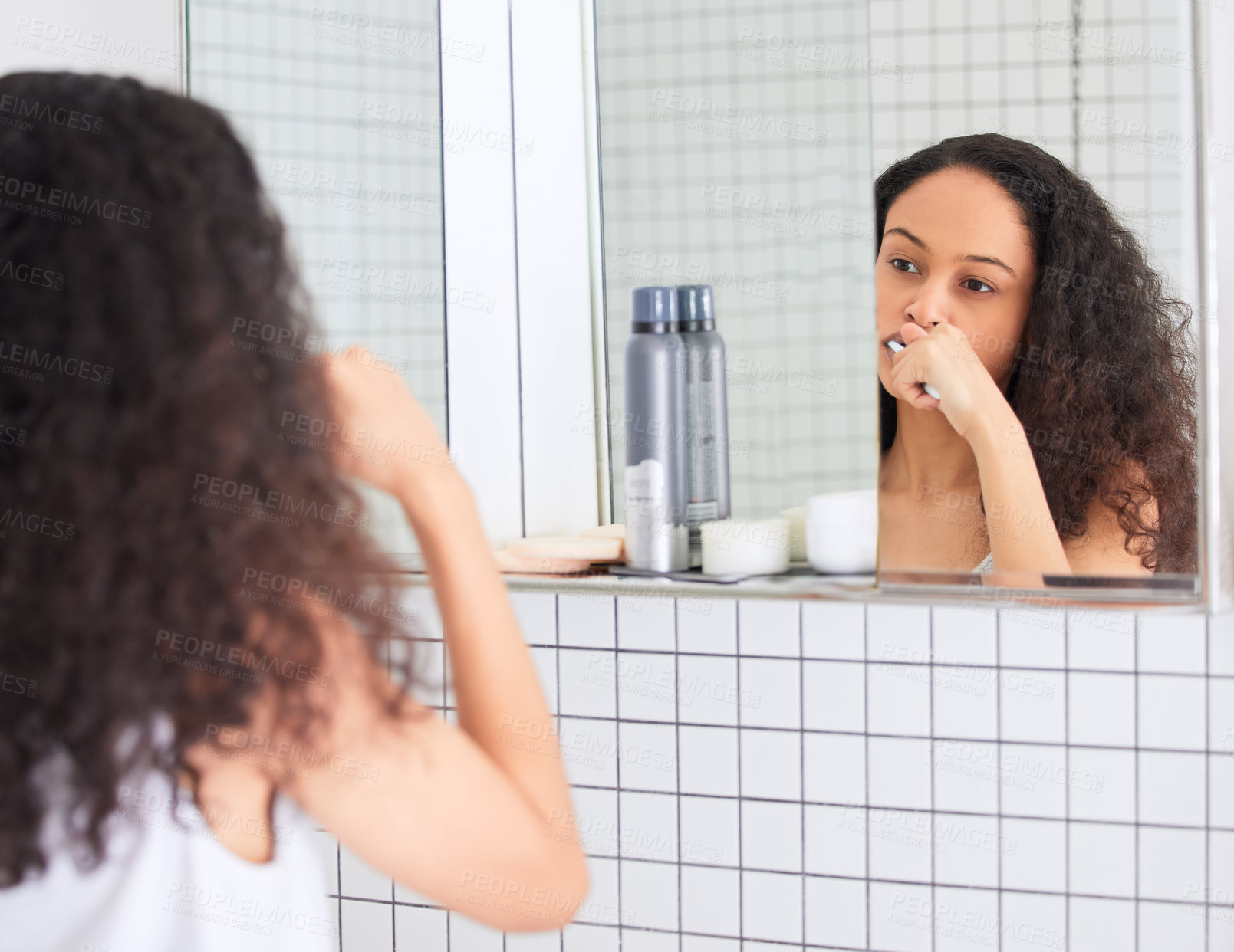 Buy stock photo Shot of an attractive young woman standing alone in her bathroom at home and brushing her teeth in the morning