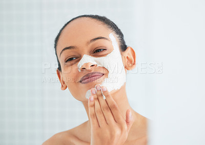 Buy stock photo Shot of an attractive young woman standing alone in her bathroom at home and applying a face mask