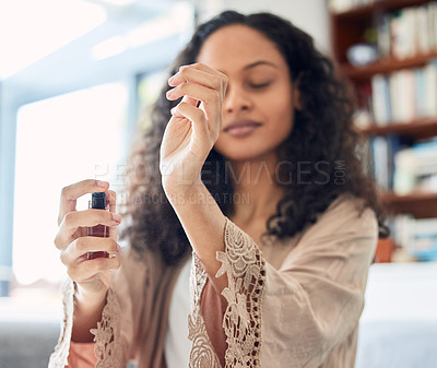 Buy stock photo Shot of an attractive young woman standing alone at home and spraying perfume in the morning