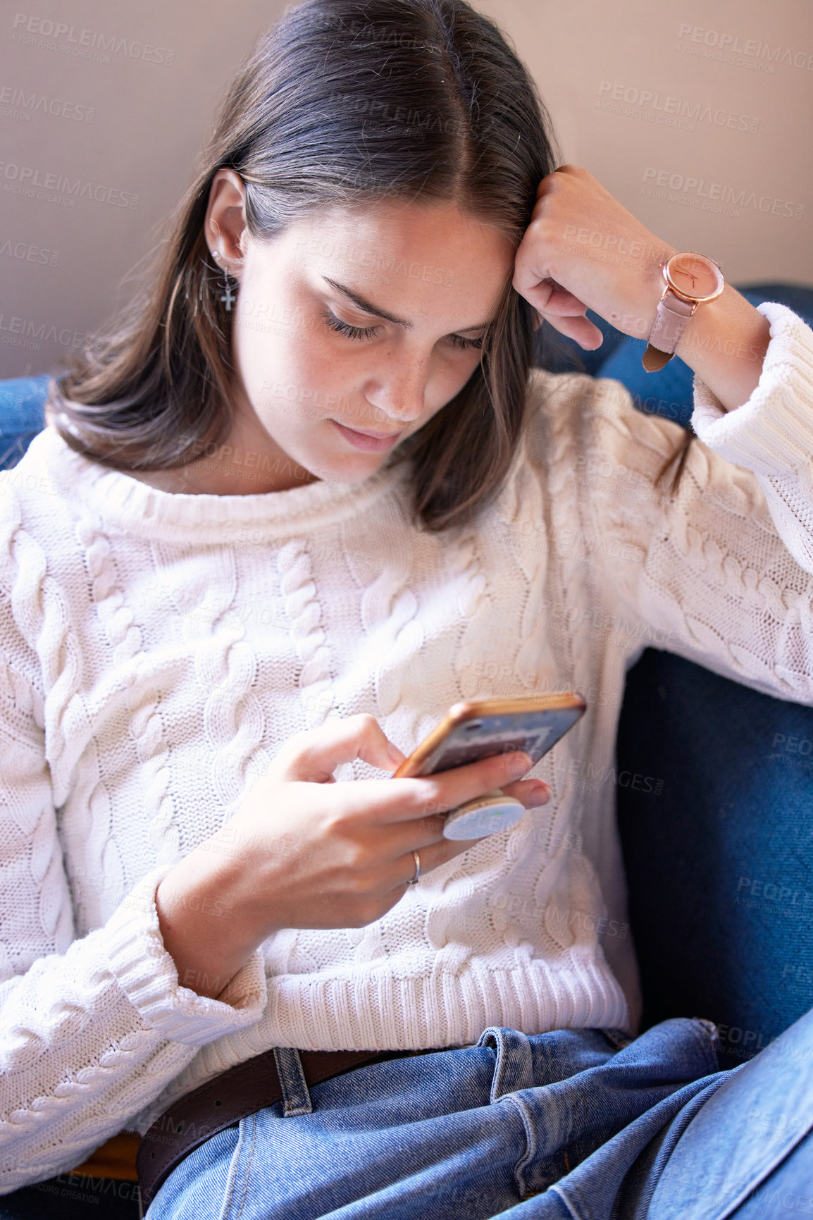 Buy stock photo Shot of a young woman sitting on her couch using her smartphone