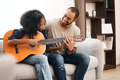 Buy stock photo Shot of a young girl learning to play the guitar with her father at home
