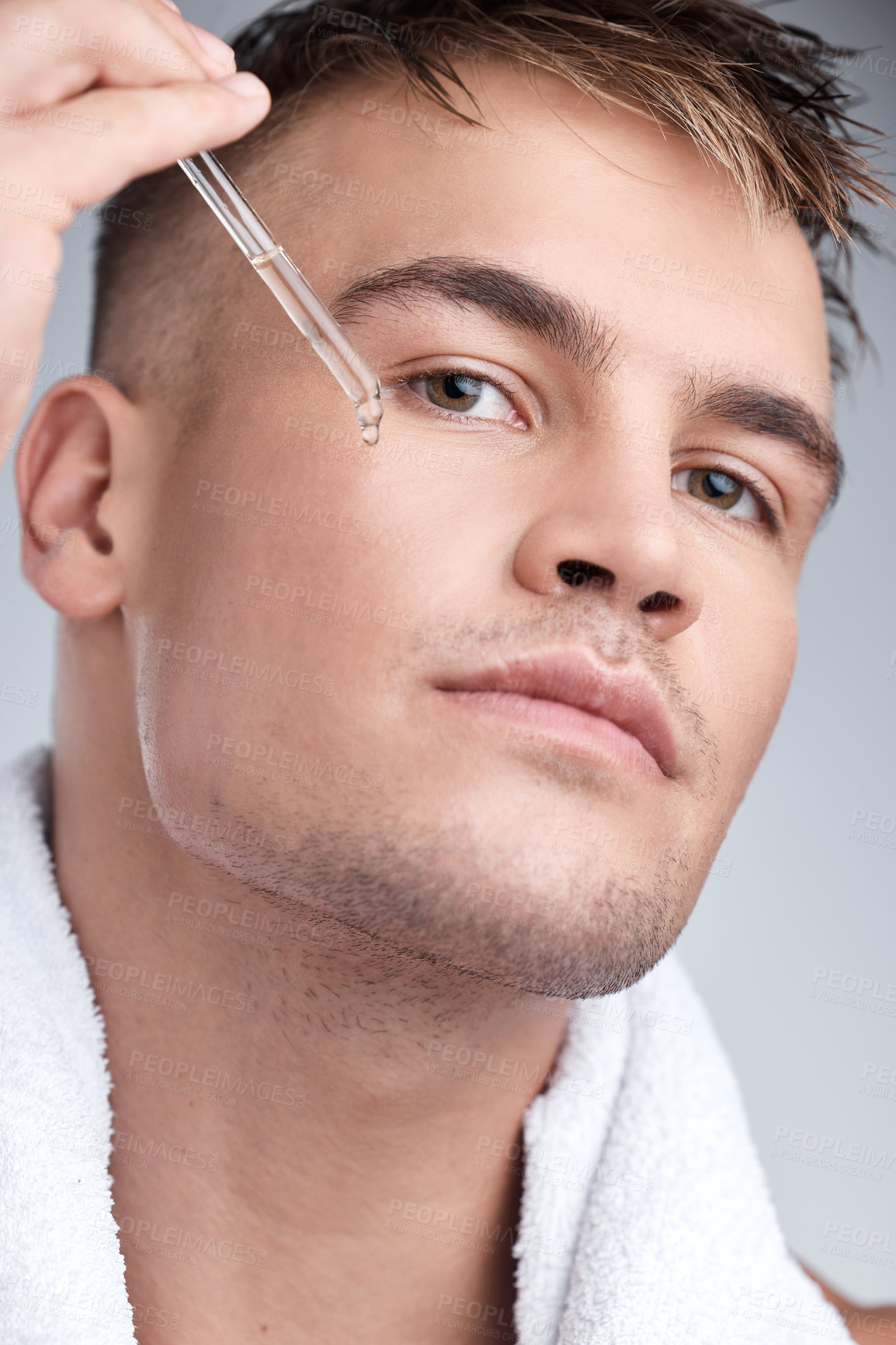 Buy stock photo Closeup shot of a young handsome man applying serum to his face against a grey background