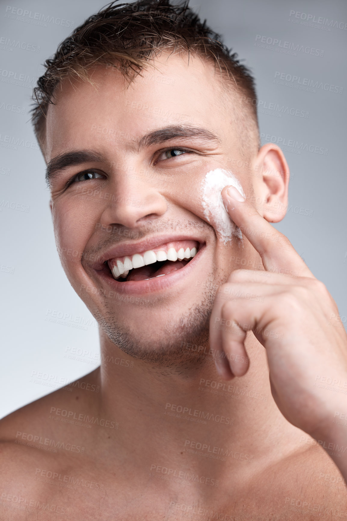 Buy stock photo Cropped closeup shot of an attractive young man applying moisturiser to his face against a grey background