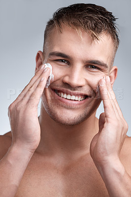 Buy stock photo Cropped closeup portrait of an attractive young man applying moisturiser to his face against a grey background