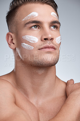 Buy stock photo Cropped closeup shot of an attractive young man applying moisturiser to his face against a grey background