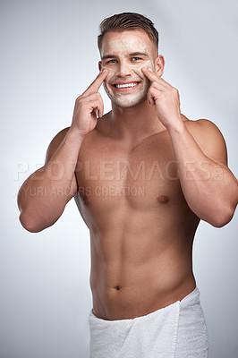 Buy stock photo Studio portrait of an attractive young man applying a beauty treatment to his face against a grey background