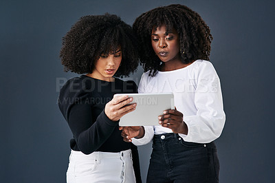 Buy stock photo Shot of two businesswomen using a digital tablet against a studio background