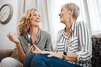 Buy stock photo Shot of two female friends using a smartphone to listen to music