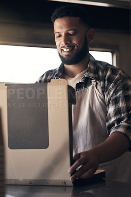 Buy stock photo Shot of a handsome young man standing alone inside his restaurant and folding pizza boxes