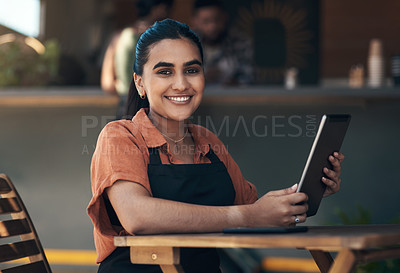 Buy stock photo Shot of an attractive young woman sitting outside her restaurant and using a digital tablet