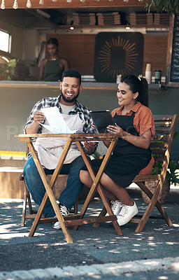 Buy stock photo Full length shot of two young restaurant owners sitting outside together and using a digital tablet to plan their menu