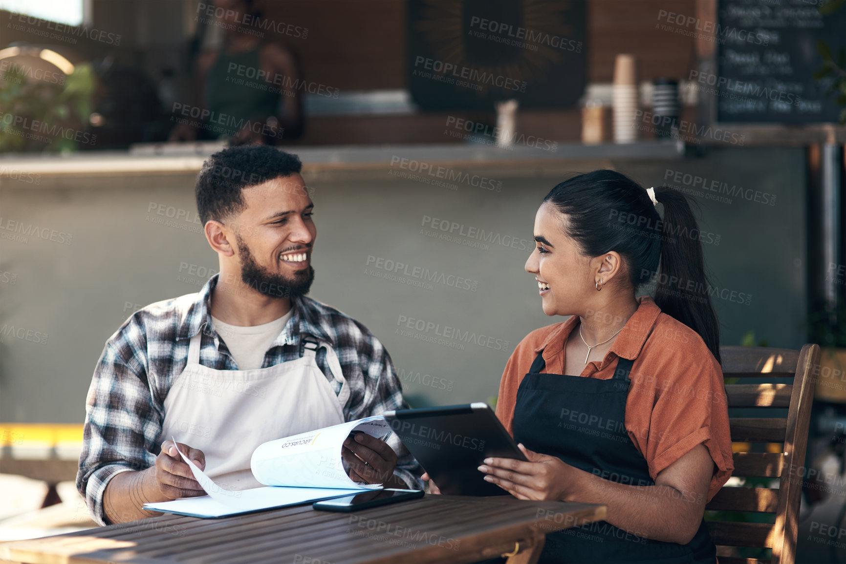 Buy stock photo Shot of two young restaurant owners sitting outside together and using a digital tablet to plan their menu