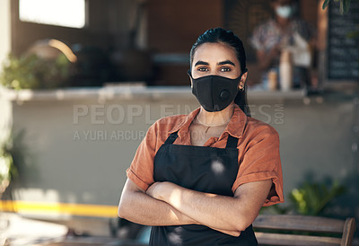 Buy stock photo Shot of a young woman standing outside her restaurant with her arms folded while wearing a face mask