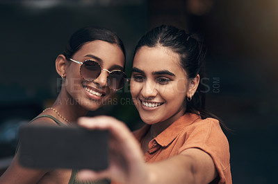 Buy stock photo Shot of two young friends standing outside a restaurant and using a cellphone to take a selfie