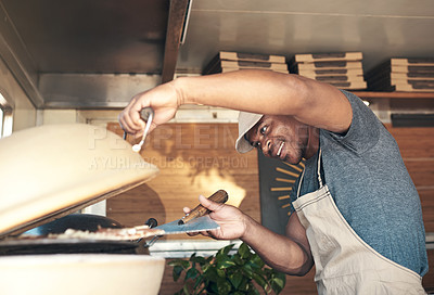 Buy stock photo Shot of a handsome young man standing alone and putting a pizza in the oven at his restaurant