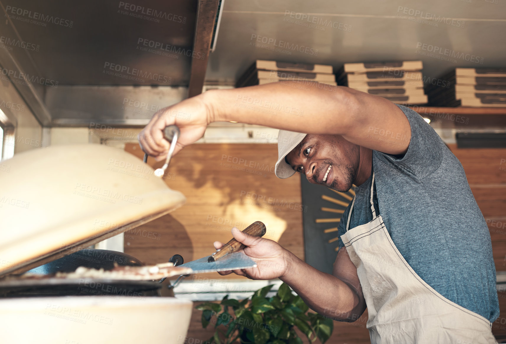 Buy stock photo Shot of a handsome young man standing alone and putting a pizza in the oven at his restaurant