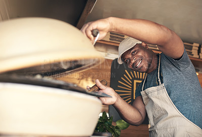 Buy stock photo Shot of a handsome young man standing alone and putting a pizza in the oven at his restaurant