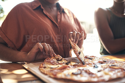 Buy stock photo Cropped shot of two unrecognizable women sitting together and enjoying a freshly made pizza at a restaurant