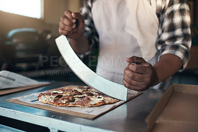 Buy stock photo Cropped shot of an unrecognizable man standing and preparing a freshly made pizza for takeaway in his restaurant