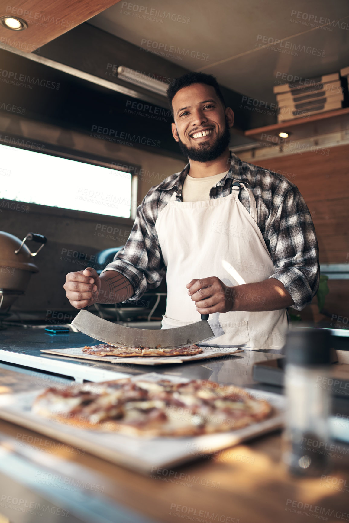 Buy stock photo Shot of a handsome young man standing and preparing a freshly made pizza for takeaway in his restaurant