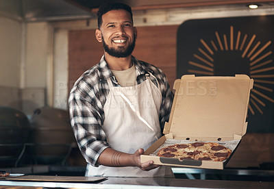 Buy stock photo Shot of a handsome young man standing alone and holding a freshly made pizza in his restaurant