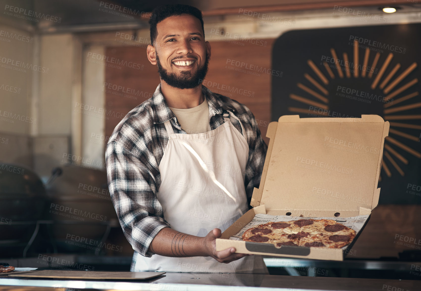 Buy stock photo Shot of a handsome young man standing alone and holding a freshly made pizza in his restaurant