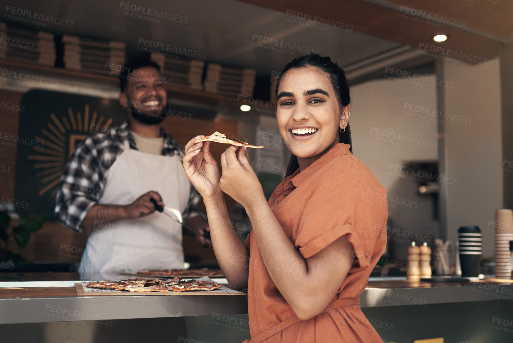 Buy stock photo Shot of an attractive young woman standing and enjoying a freshly made pizza at a restaurant