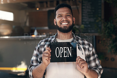 Buy stock photo Shot of a handsome young man standing outside his restaurant and holding an open sign