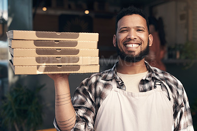 Buy stock photo Shot of a handsome young man standing outside his restaurant and holding a stack of pizza boxes