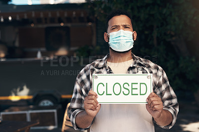 Buy stock photo Shot of a young man standing outside his restaurant and wearing a face mask while holding a closed sign