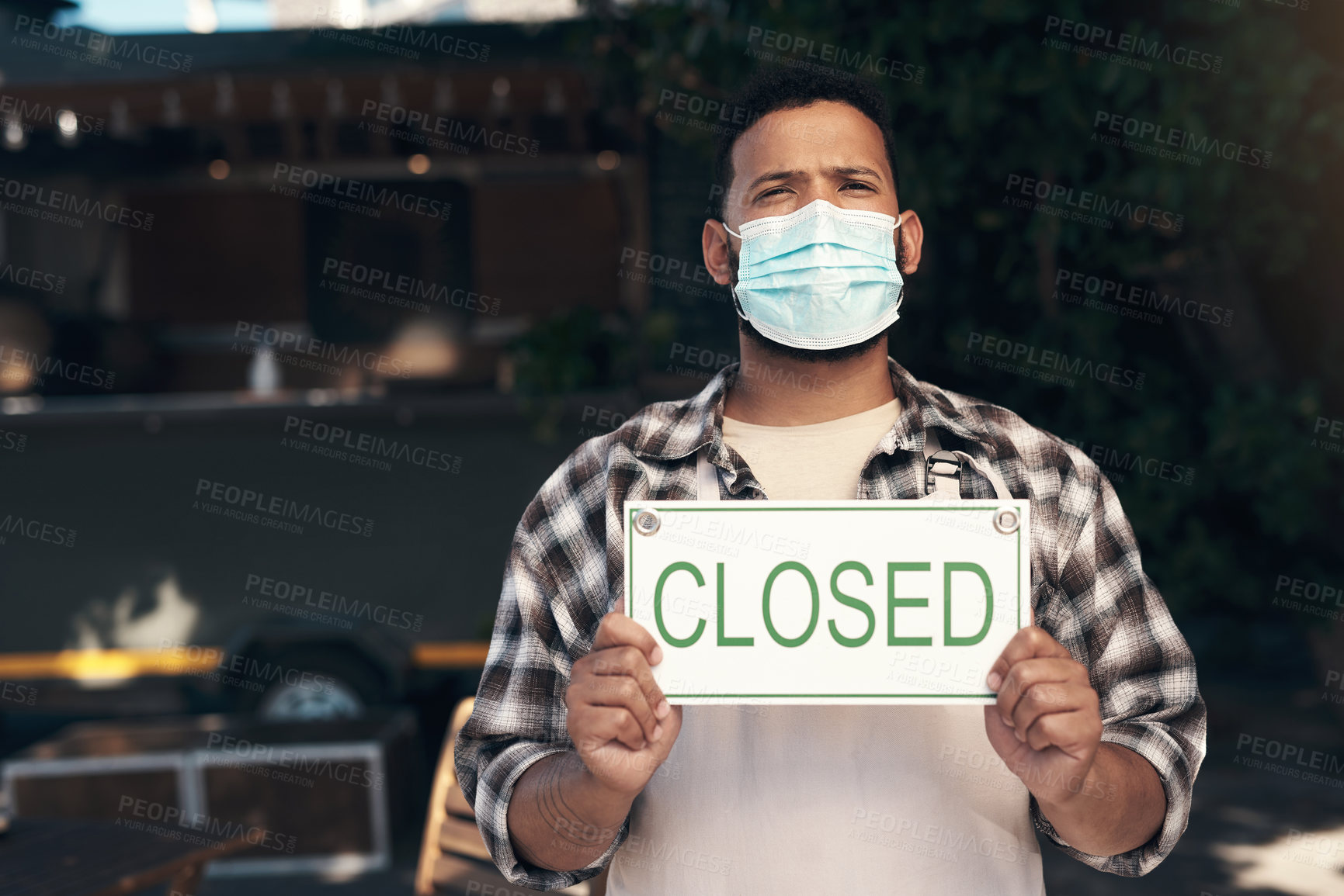 Buy stock photo Shot of a young man standing outside his restaurant and wearing a face mask while holding a closed sign