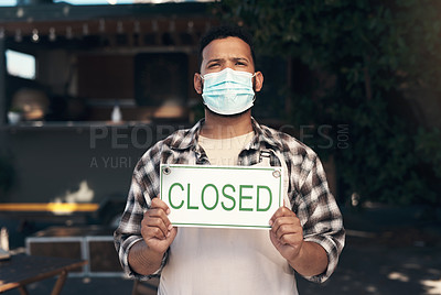 Buy stock photo Shot of a young man standing outside his restaurant and wearing a face mask while holding a closed sign