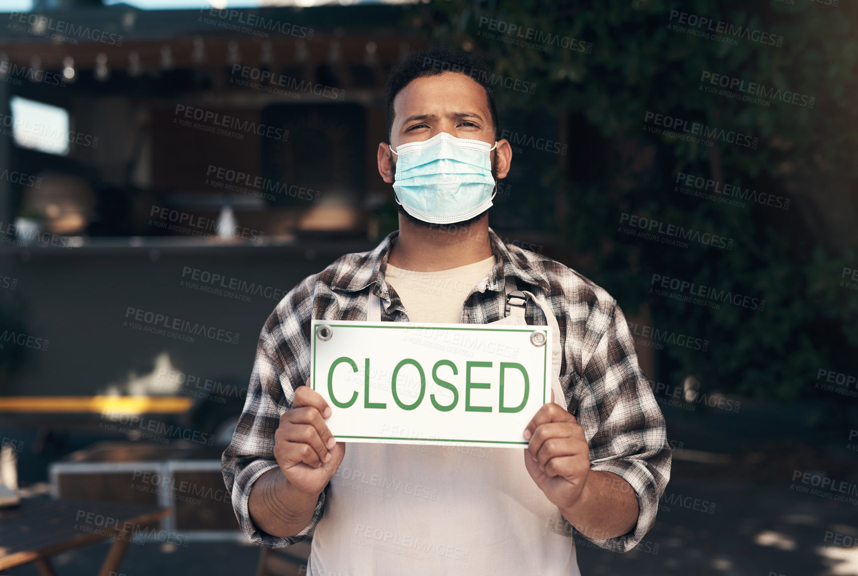 Buy stock photo Shot of a young man standing outside his restaurant and wearing a face mask while holding a closed sign