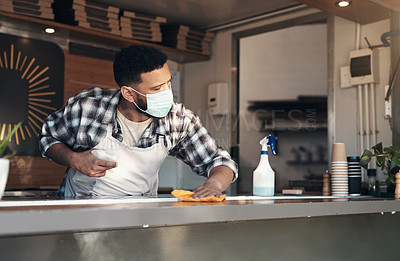 Buy stock photo Shot of a young man standing alone and sanitising the counter tops in his restaurant while wearing a face mask