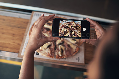 Buy stock photo Cropped shot of an unrecognizable woman sitting alone and using her cellphone to photograph her pizza at a restaurant