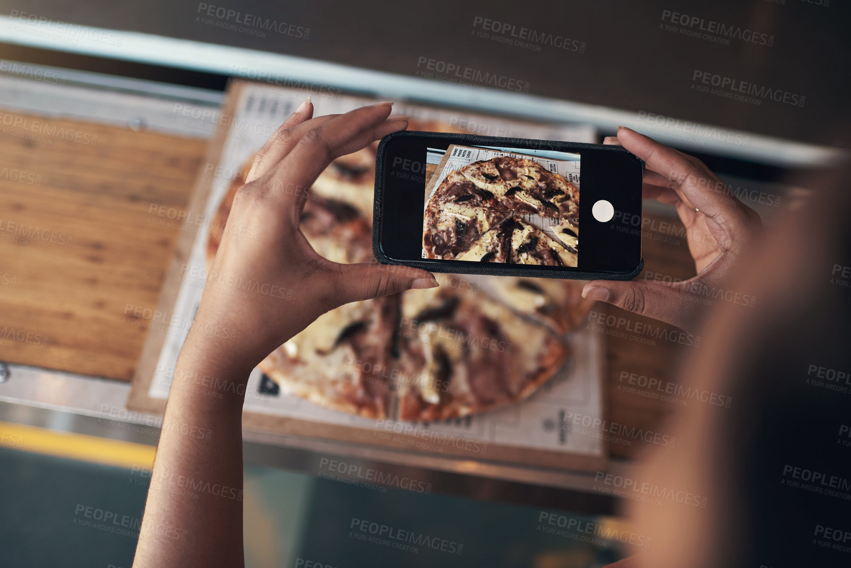 Buy stock photo Cropped shot of an unrecognizable woman sitting alone and using her cellphone to photograph her pizza at a restaurant