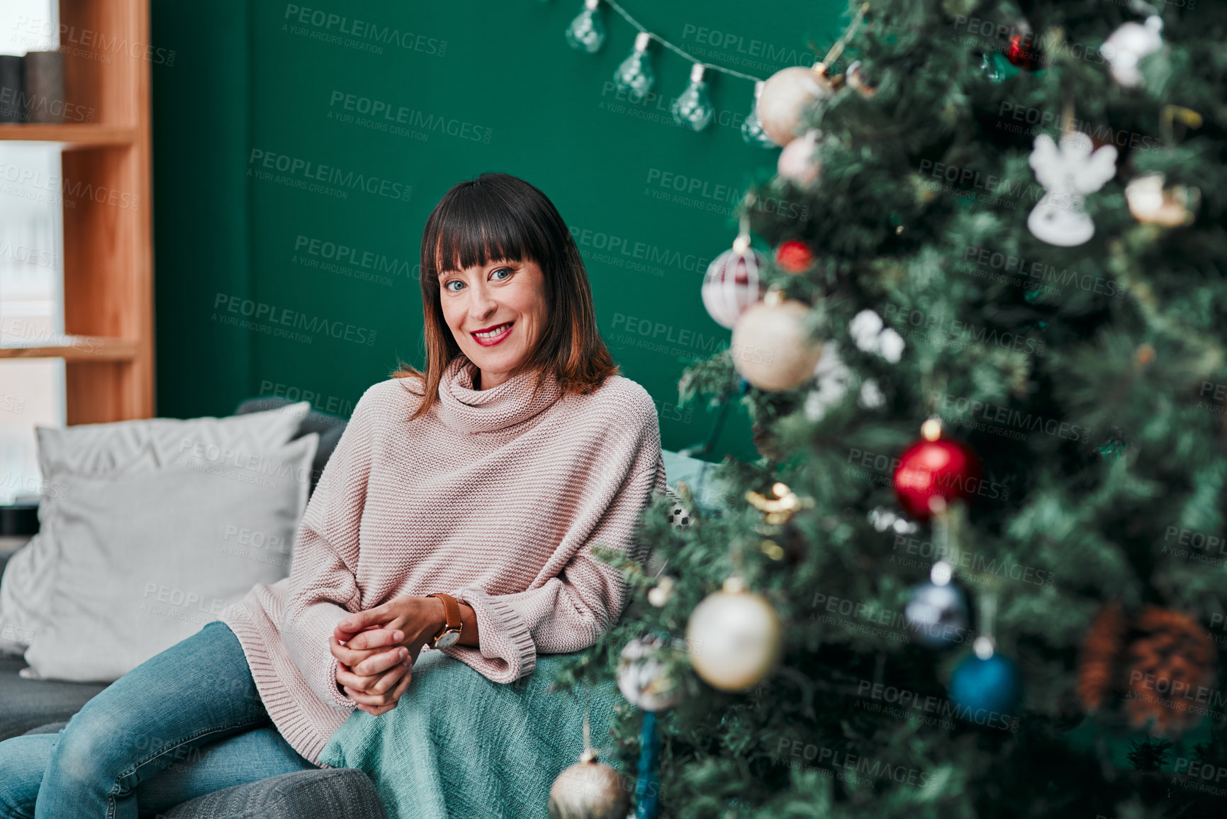Buy stock photo Portrait o a young an attractive woman relaxing on the sofa next to a Christmas tree at home