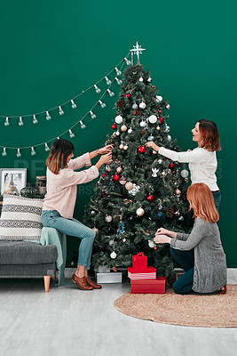 Buy stock photo Shot of three attractive women decorating a Christmas tree together at home