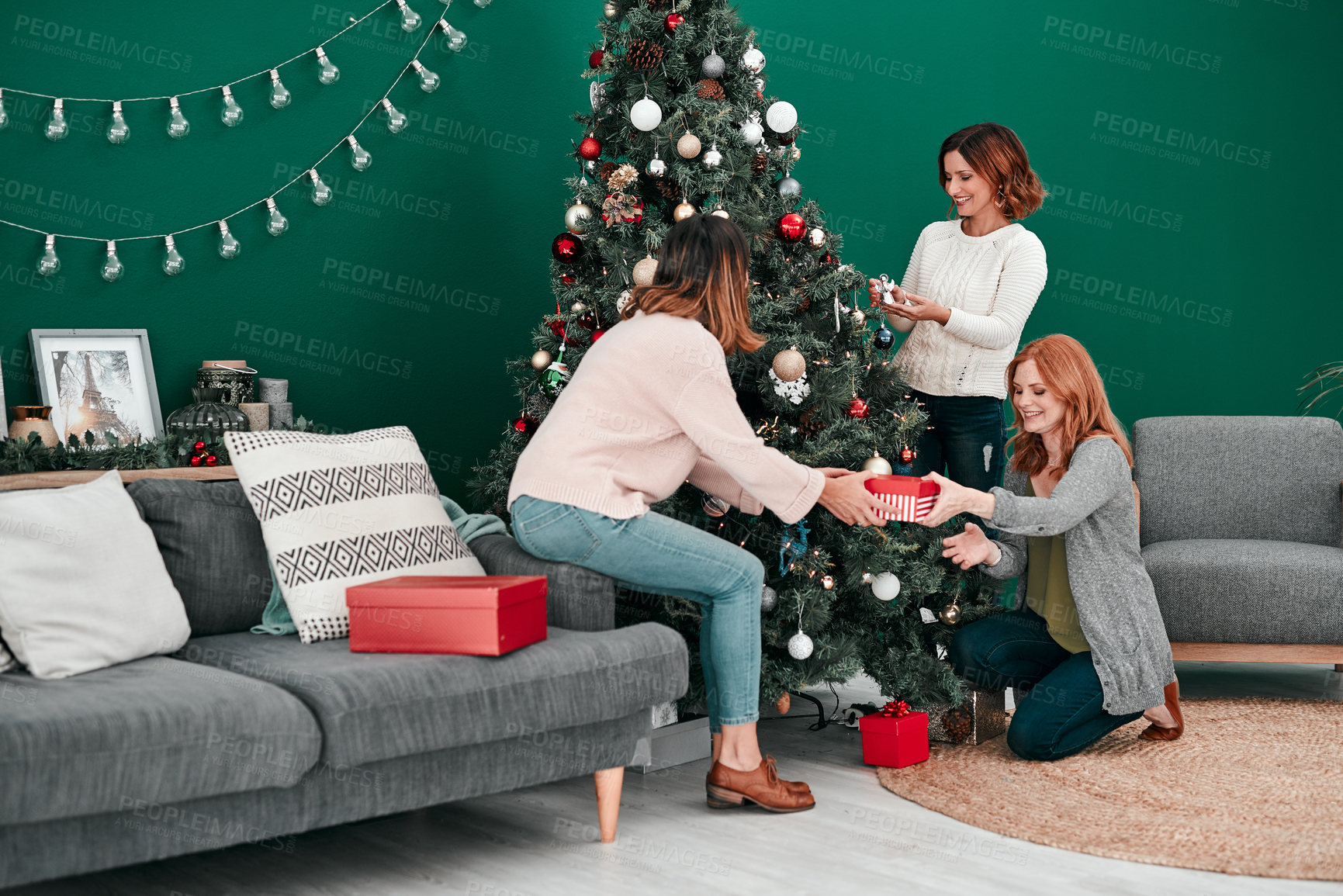 Buy stock photo Shot of three attractive women decorating a Christmas tree together at home