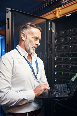 Buy stock photo Shot of a mature man using a laptop while working in a server room