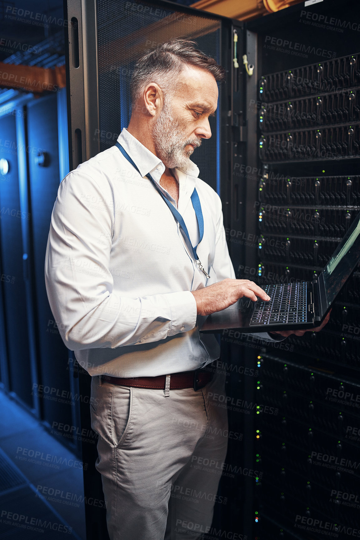 Buy stock photo Shot of a mature man using a laptop while working in a server room