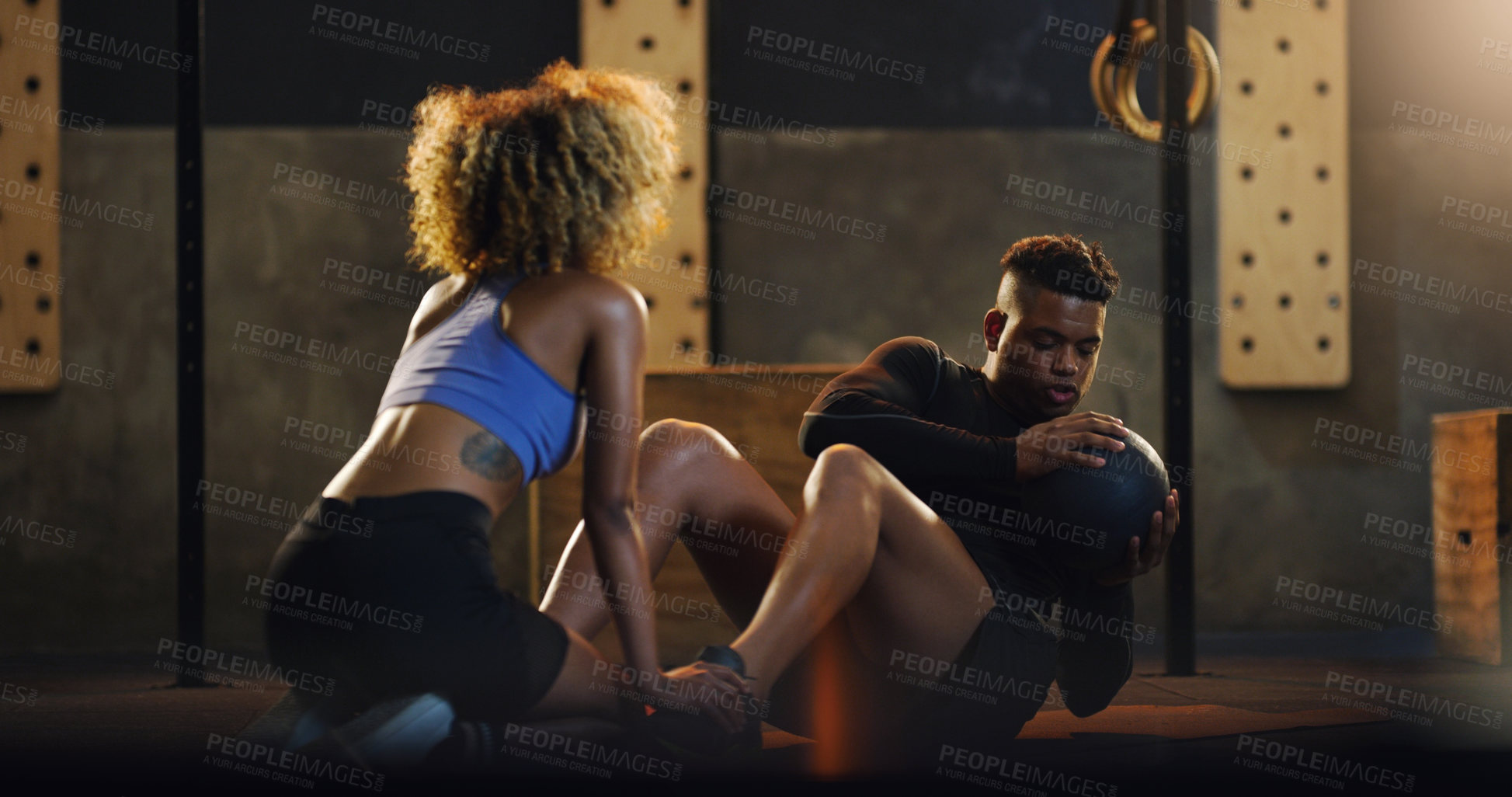 Buy stock photo Shot of a young man doing russian twists with a weighted ball and the help of a trainer in a gym