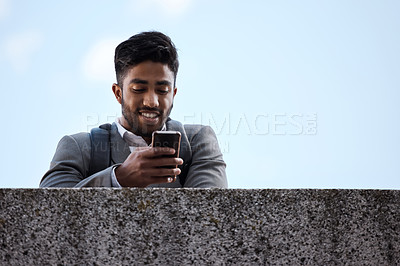 Buy stock photo Phone, networking and businessman by a wall in the city browsing on social media or mobile app. Happy, smile and professional male employee scrolling on the internet while waiting for a cab in town.