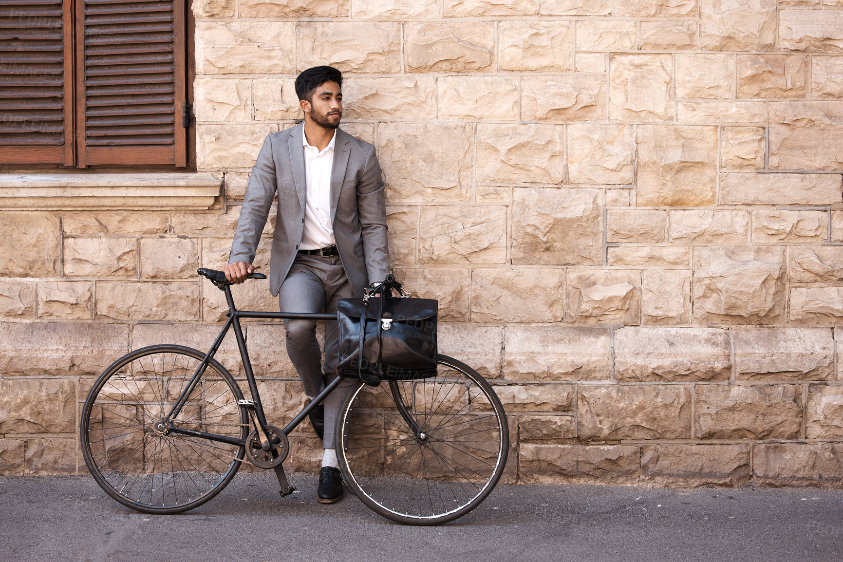 Buy stock photo Bicycle, suit and businessman in the city for travel standing by a brick wall building. Briefcase, professional and young male employee riding a bike or commuting to his work office in an urban town.